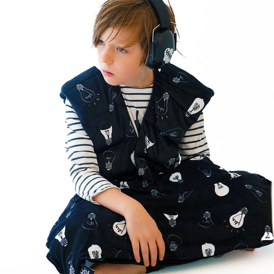 A child wearing black with a pattern of light bulbs and other sensory items, including a denim sack with the product name &