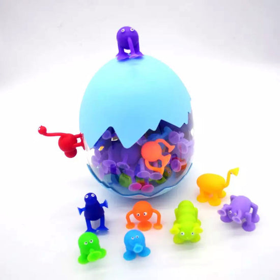 An assortment of colorful silicone suction toys designed to stick to smooth surfaces, displayed both inside an egg-shaped container and on a flat surface.