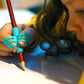 A child is drawing with a pencil that has a blue silicone pencil grip attached to the top.