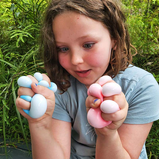 A child holding two pocket-sized sensory stress balls in blue and pink colors.