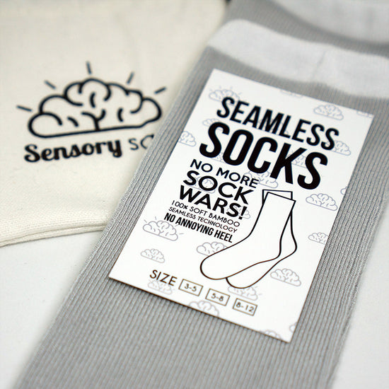 Packaging of Sensory Sam seamless socks in grey with a white band, displaying the product name and emphasizing no heel and seamless technology.
