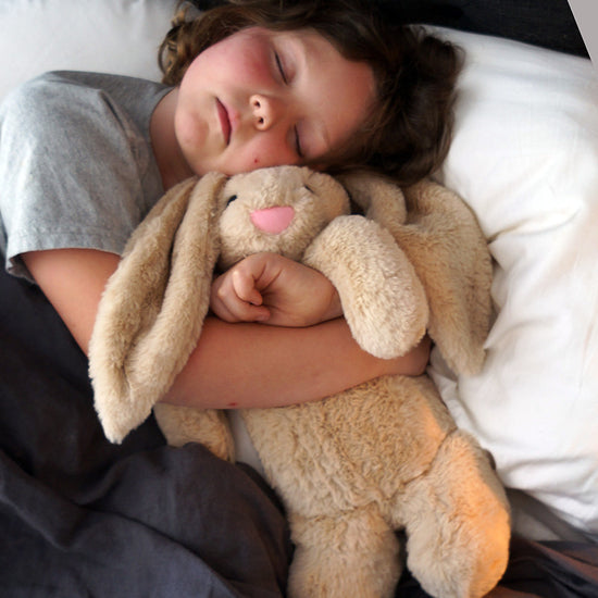 A child sleeping with a beige, plush, weighted bunny toy.