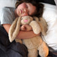 A child sleeping with a beige, plush, weighted bunny toy.