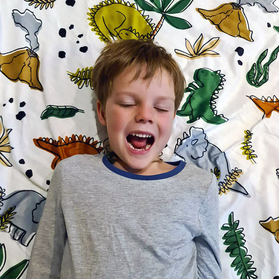 A child lying on a weighted blanket with a colorful dinosaur pattern cover.