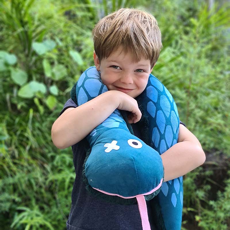 A child embracing a blue snake-shaped weighted plush toy outdoors.
